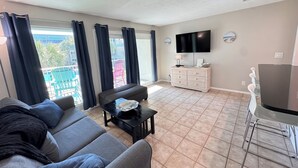 Ein Wohnzimmer mit einer Couch, einem Couchtisch, einem Fernseher, einem Schrank und einem Balkon mit Sitzgelegenheiten.