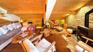 A cozy cabin interior with a wooden ceiling, a sofa, a bed, a fireplace, and a stone wall.
