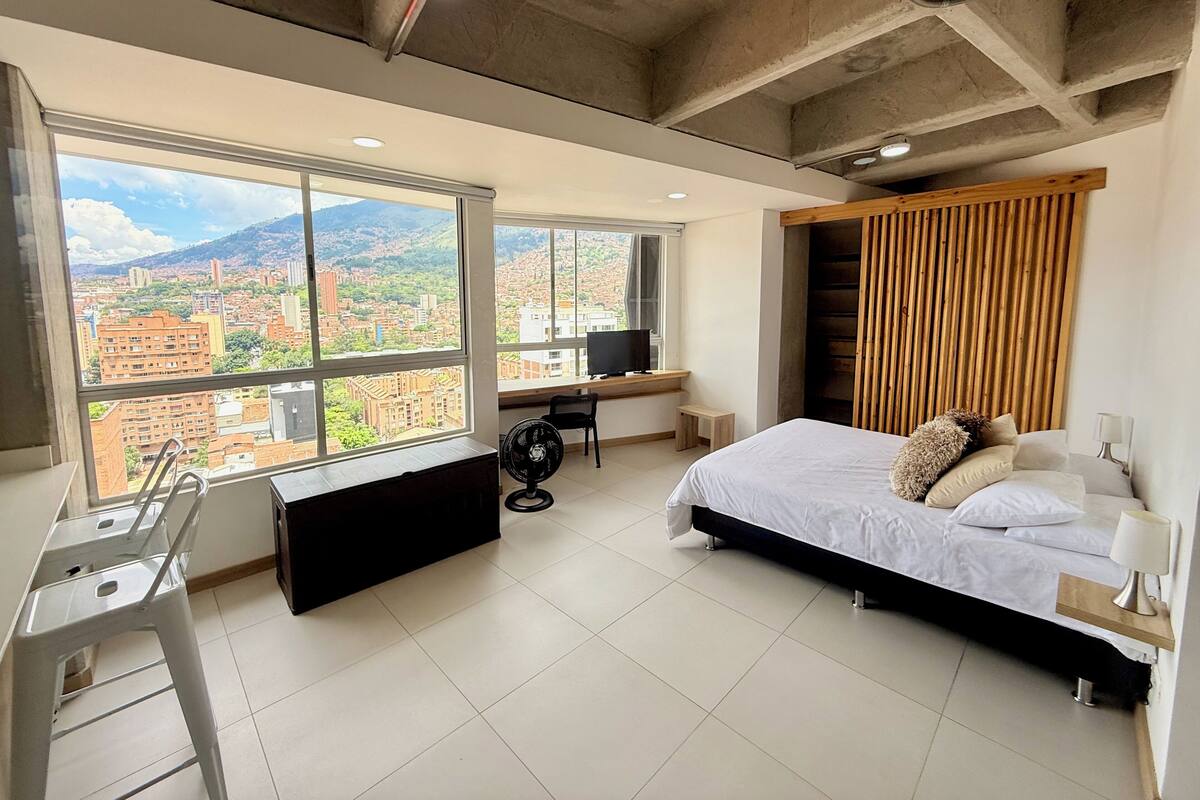 A modern bedroom with a large window, a bed, a desk, and a chair.