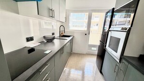 Cozinha moderna com armários cinza, bancada preta, cuba de aço inoxidável e forno embutido.