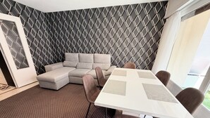 Uma sala de estar moderna com um sofá seccional, uma mesa de jantar com quatro cadeiras e um tapete estampado.