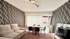 Uma sala de estar moderna com sofá, mesa de jantar e cadeiras. Há uma janela grande com vista para o exterior.