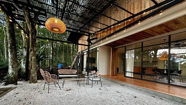 Un espace extérieur moderne, aménagé avec des meubles en osier et doté d’un luminaire suspendu original.