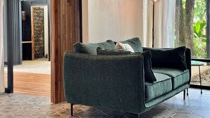 Un salon moderne avec un canapé vert foncé, une lampe et une vue sur une structure en bois à l’extérieur.