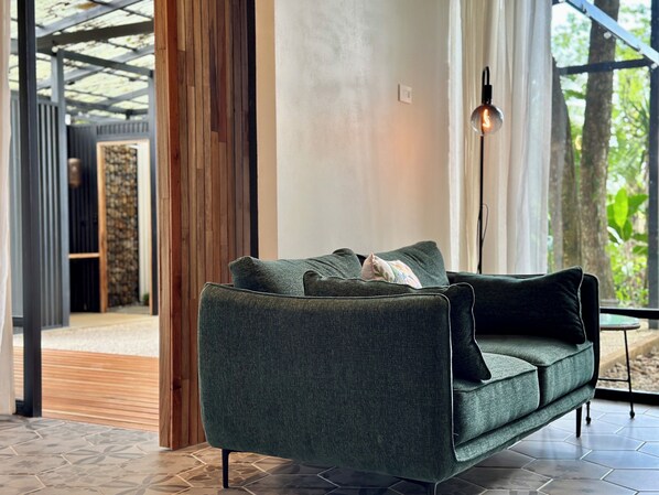 Una sala de estar moderna con un sofá verde oscuro, una lámpara y vistas de una construcción de madera.