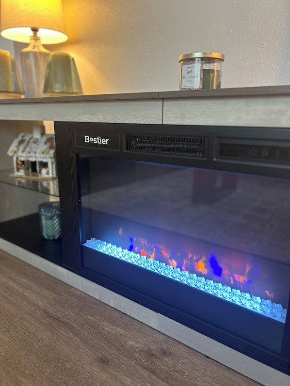A Bestier electric fireplace with a blue-lit fire effect, a lamp, and a small decorative item on the mantel.