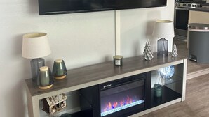 A modern living room with a mounted flat-screen TV, a fireplace, and a console table with decorative items. - 3 Bedroom - Creek Access Alaskan Blackstone Retreat (Anchorage)