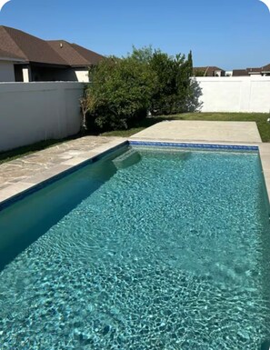 A rectangular swimming pool with clear blue water, surrounded by a white wall and a grassy area.