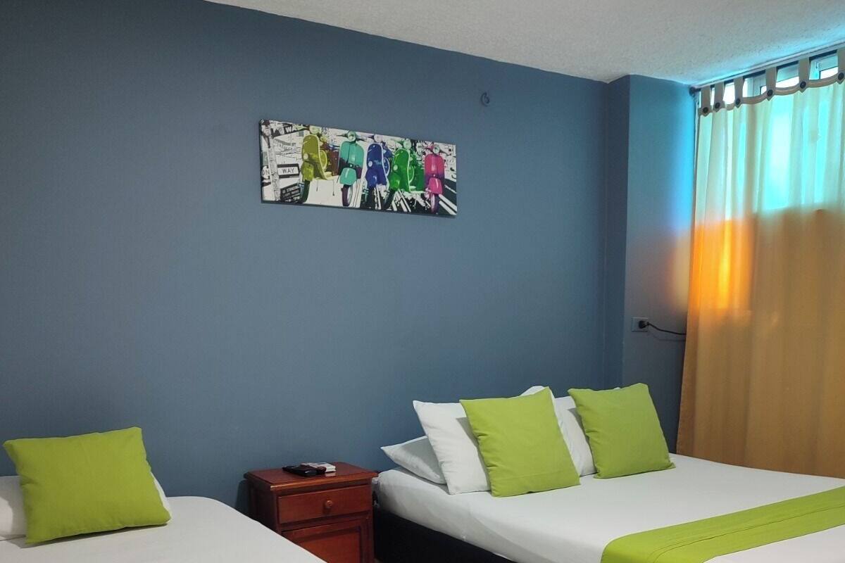 Ein Hotelzimmer mit zwei Betten, jeweils mit grün-weißer Bettwäsche, einem Nachttisch, einem Wandbild und einem Fenster mit Vorhängen.
