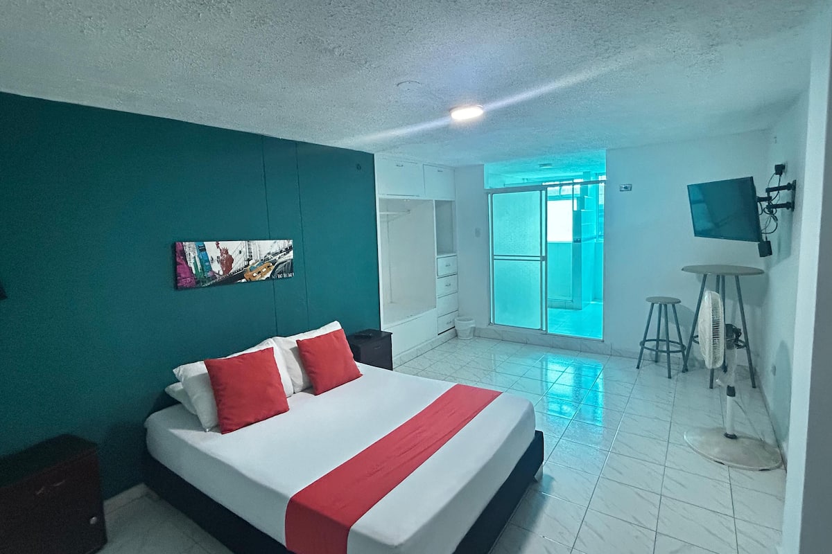 Ein Hotelzimmer mit einem groĂźen Bett, einem an der Wand montierten Fernseher und Blick durch eine GlastĂĽr nach drauĂźen.
