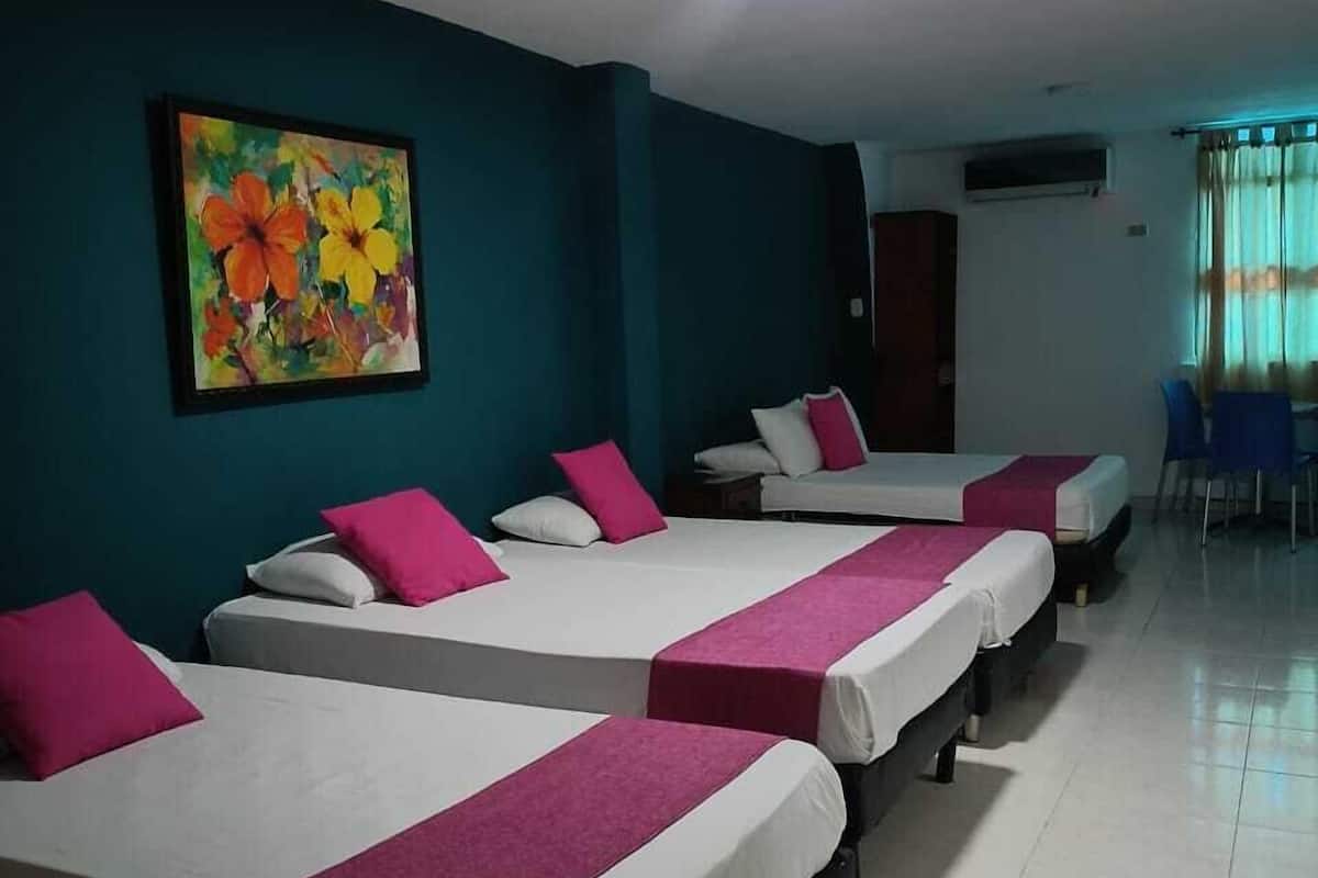 Ein Hotelzimmer mit vier Betten, jedes mit weißer Bettwäsche und pinkfarbenen Akzenten. Darüber hängt ein farbenfrohes Bild an der Wand.