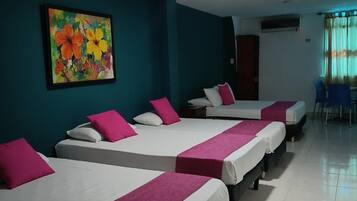 Een hotelkamer met vier bedden, elk voorzien van witte beddengoed en roze accenten. Boven de bedden hangt een kleurrijk schilderij.