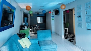 Eine Hotellobby mit einem blauen Sofa, einem Wasserspender, einem Fernseher und einem Schachbrettmuster-Boden.
