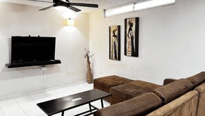 A modern living room with a flat-screen TV, a ceiling fan, a brown leather sofa, and two framed artworks on the wall. - Hotel Boston Superior (Barranquilla)