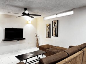 A modern living room with a flat-screen TV, a ceiling fan, a brown leather sofa, and two framed artworks on the wall. - Hotel Boston Superior (Barranquilla)