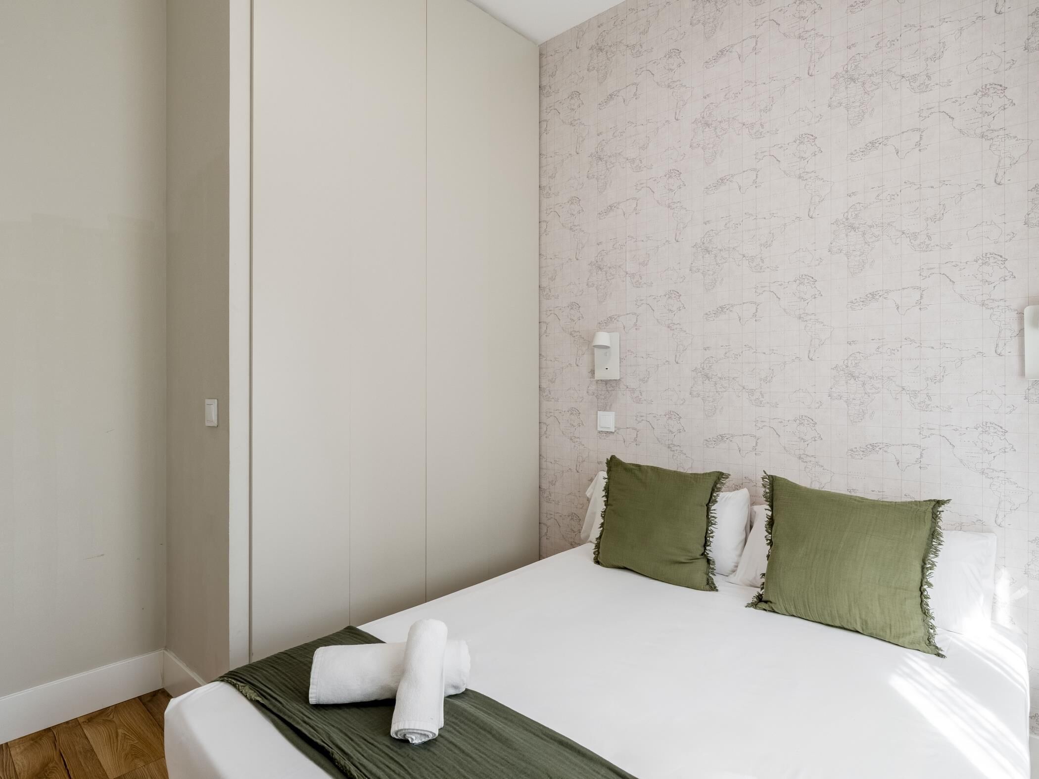 Une chambre d’hôtel avec un lit, des oreillers verts et une serviette pliée posée sur le lit.