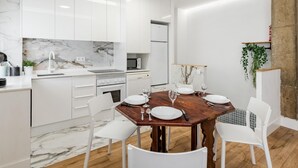 A modern kitchen with white cabinets, a marble backsplash, and a dining area with a wooden table set for four.