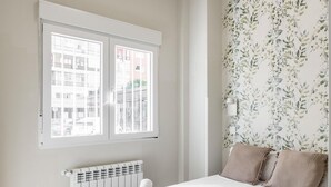 A bedroom with a large bed, a radiator, and a window with a view of buildings.