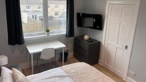 A bedroom with a bed, a desk, a chair, a TV, and a door.