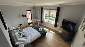 Et moderne soveværelse med seng, sengebord, fjernsyn og et vindue med udsigt til gaden.
