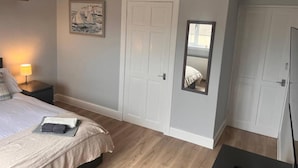 A bedroom with a bed, bedside table, lamp, and a mirror.
