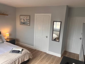 Een slaapkamer met een bed, nachtkastje, lamp en spiegel.