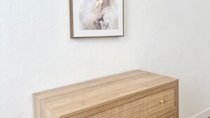 Une peinture abstraite encadrée sur un mur blanc à texture, une console en bois avec un panier tressé, et un mur blanc uni.
