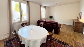 Une pièce avec une table de salle à manger ronde, des chaises, un canapé rouge, un petit téléviseur posé sur un meuble et un plancher en bois.