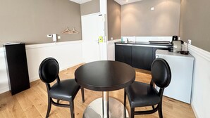 A compact room with a round table and two chairs, a kitchenette with a sink, and a door leading to another room. - T2 rénové & design – Comme à l'hotel ! (Lorient)