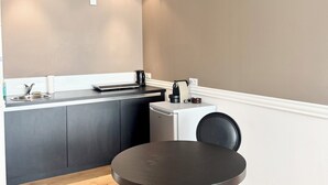 A compact kitchen with a sink, a kettle, a small refrigerator, and a round table with a chair. - T2 rénové & design – Comme à l'hotel ! (Lorient)