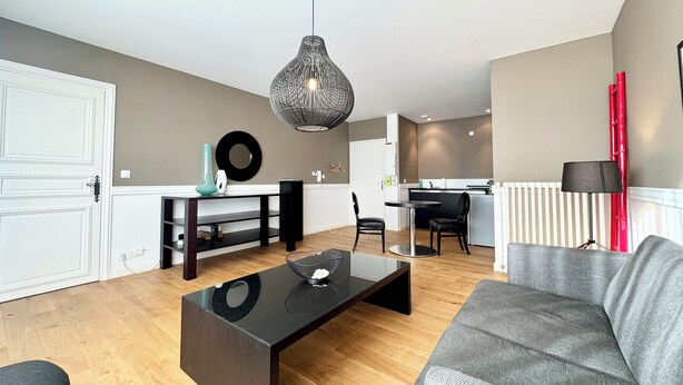 A modern living room with a black coffee table, grey sofa, and a dining area with a white table and chairs. - T2 rénové & design – Comme à l'hotel ! (Lorient)