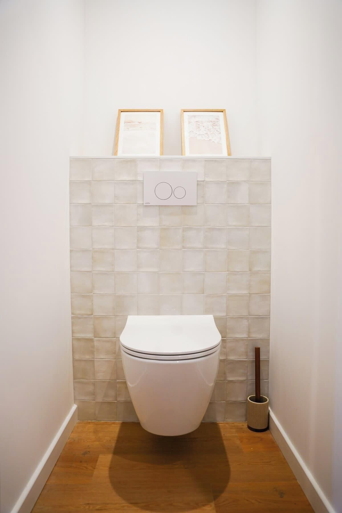 Un baño pequeño y moderno con inodoro blanco, pared con azulejos y suelo de madera.