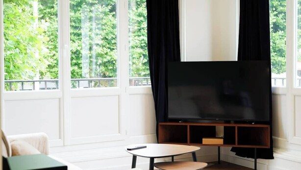Una sala de estar moderna con un televisor de pantalla plana grande, un sofá color beige, una mesita redonda pequeña y una silla negra.
