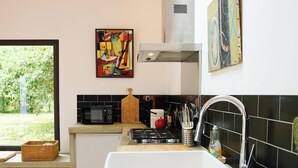 Una cocina moderna con un lavamanos grande blanco, salpicadero de azulejos negros y encimeras de madera. Hay una ventana que ofrece vistas a la vegetación exterior.