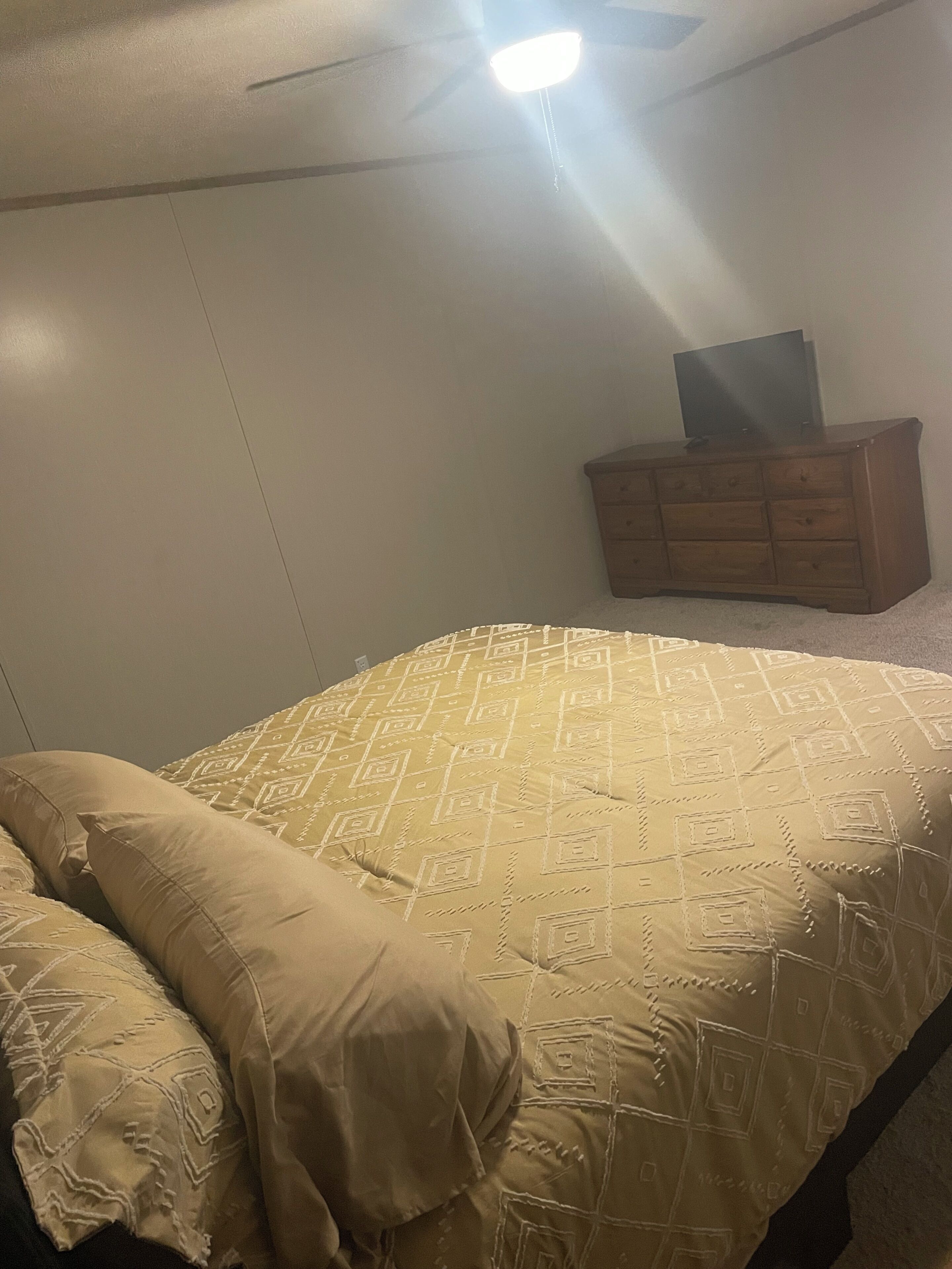 A bedroom with a bed, a dresser, and a ceiling fan.
