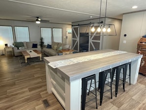 A modern kitchen with a central island, bar stools, and a dining area with a sofa and coffee table.