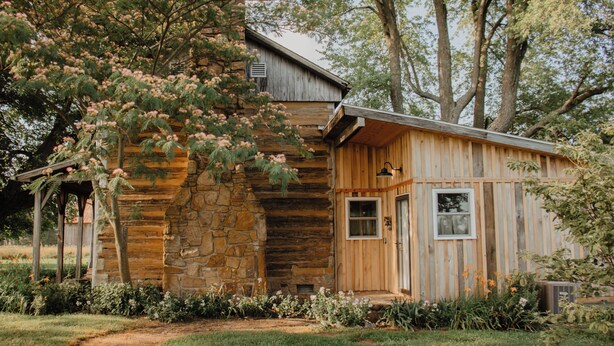 A rustic cabin with a stone foundation, wooden siding, and a covered porch. - Rustic 1800s' Log Cabin with Modern Amenities on an Old Farm close to Owensboro (Utica)
