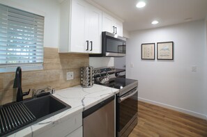 Una cocina moderna con armarios blancos, electrodomésticos de acero inoxidable, un microondas integrado y un hervidor.