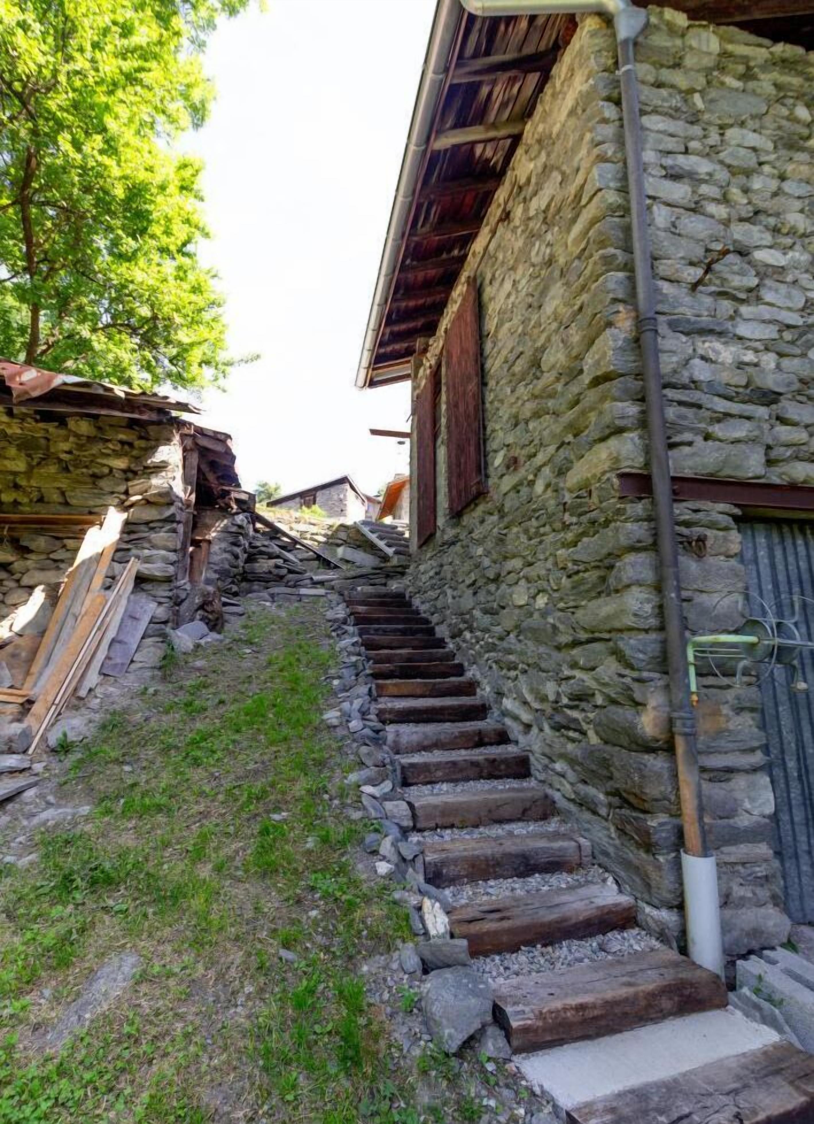 A stone staircase leading up to a rustic building with wooden steps and a metal gutter.