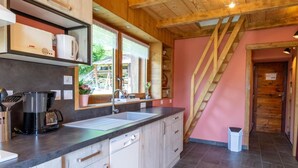 A modern kitchen with a large window, wooden ceiling beams, and a staircase leading to another room.