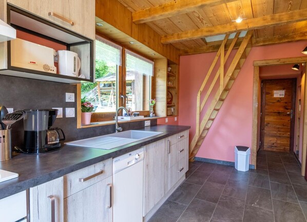 Una cocina moderna con un ventanal grande, vigas de techo de madera y una escalera que lleva a otra habitación.