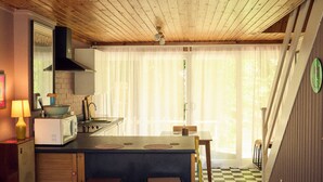Een kleine keuken met een magnetron, kookplaat en gootsteen, een eethoek met een tafel en stoelen, en een vloer met een geruit patroon.