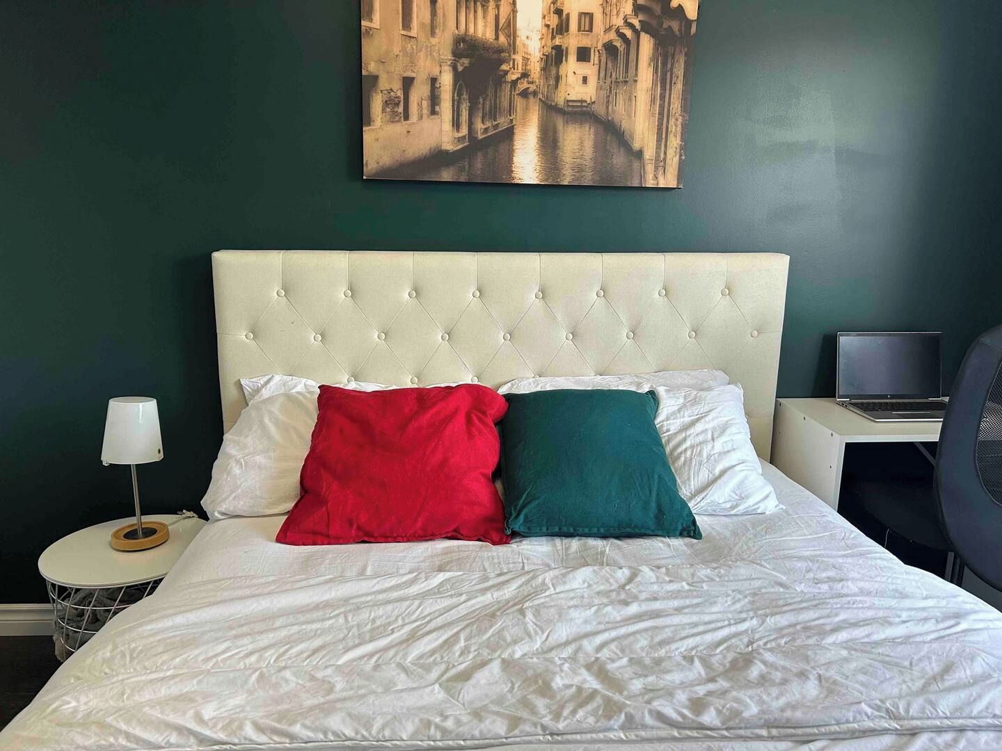 Une chambre d’hôtel avec un lit, un ordinateur portable posé sur un bureau et un tableau accroché au mur.