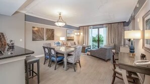 Habitación de hotel moderna con zona de comedor, sofá y balcón con cortinas.