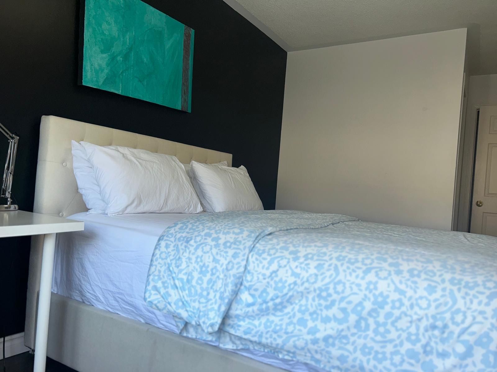 A hotel room with a bed, white headboard, and a nightstand with a lamp.
