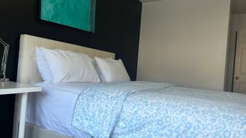 A hotel room with a bed, white headboard, and a nightstand with a lamp.