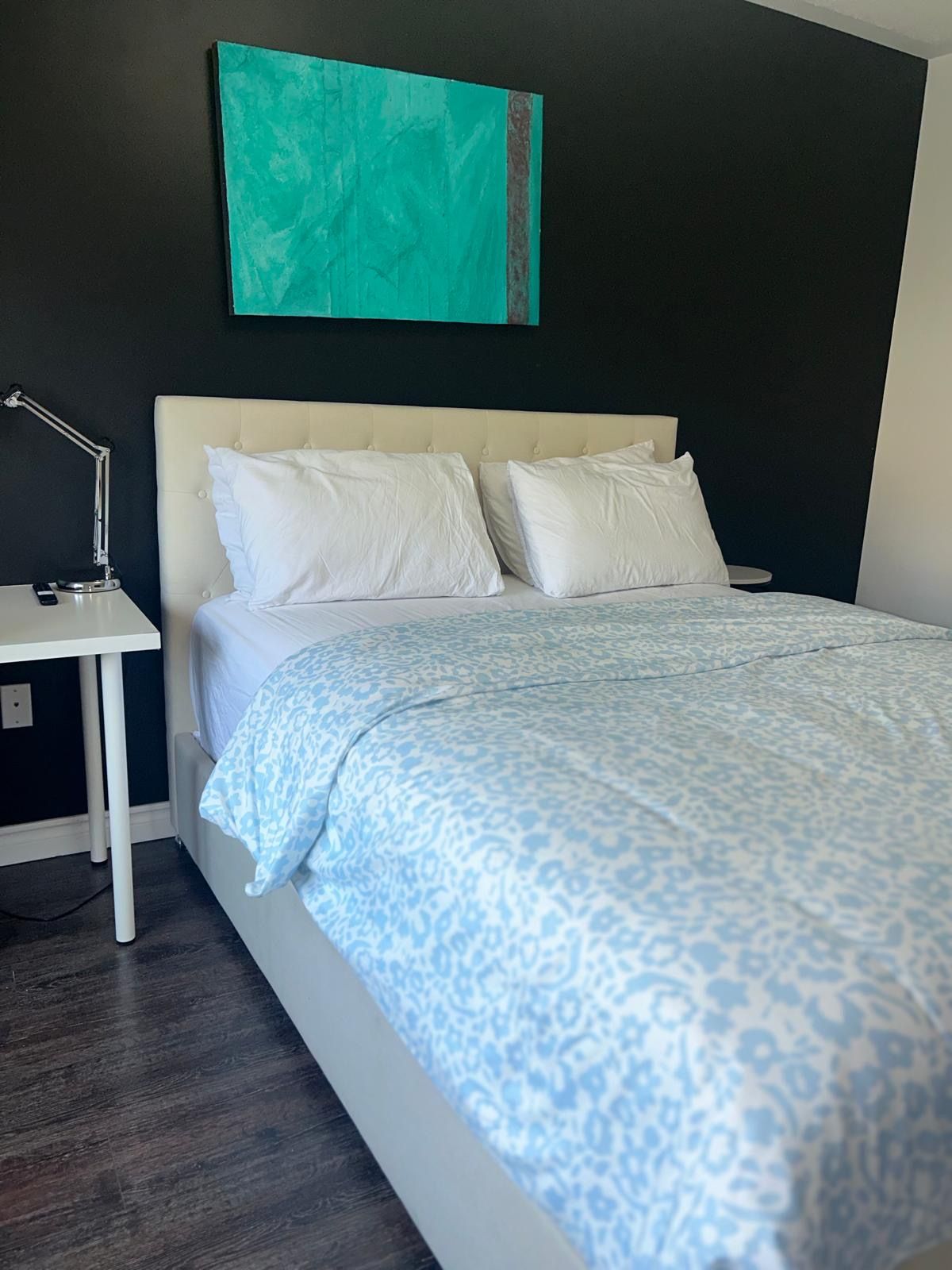 A bedroom with a bed, white nightstand, and a wall-mounted lamp.