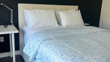 A bedroom with a bed, white nightstand, and a wall-mounted lamp.