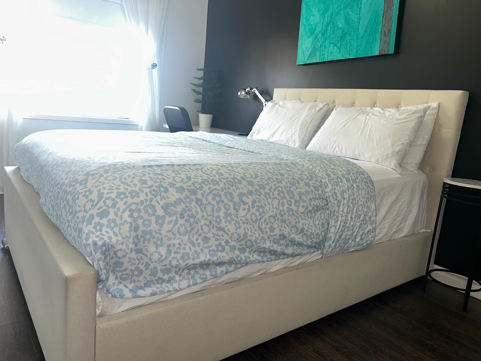 A bedroom with a bed, a chair, a desk, and a wall-mounted lamp.