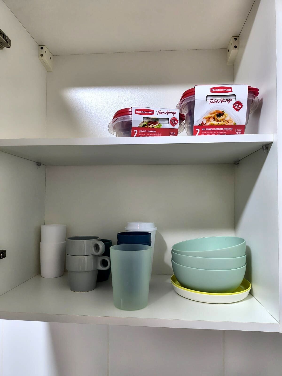 Un estante de cocina con una caja de Rubbermaid Take Alongs, un recipiente blanco y tazones apilados.